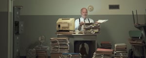 Man sitting at desk with old computer and paperwork